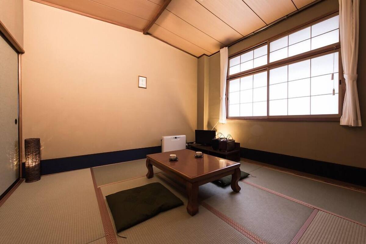 A traditional Japanese room with tatami flooring, a low table, a television, and a window with curtains.