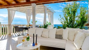 A covered outdoor seating area with a white sofa, a round table, and a view of the sea. - Villa Lucia (dubrovnik)