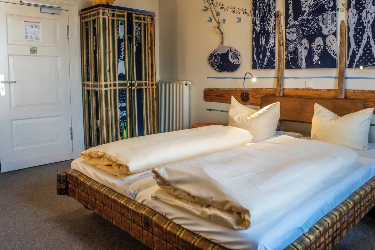 A double bed with white linens, a wooden headboard, and a small wooden stool beside it.