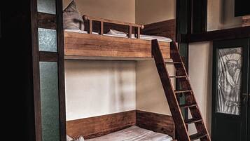 Una cama litera con escalera de madera, un estante pequeño y un cuadro en la pared.