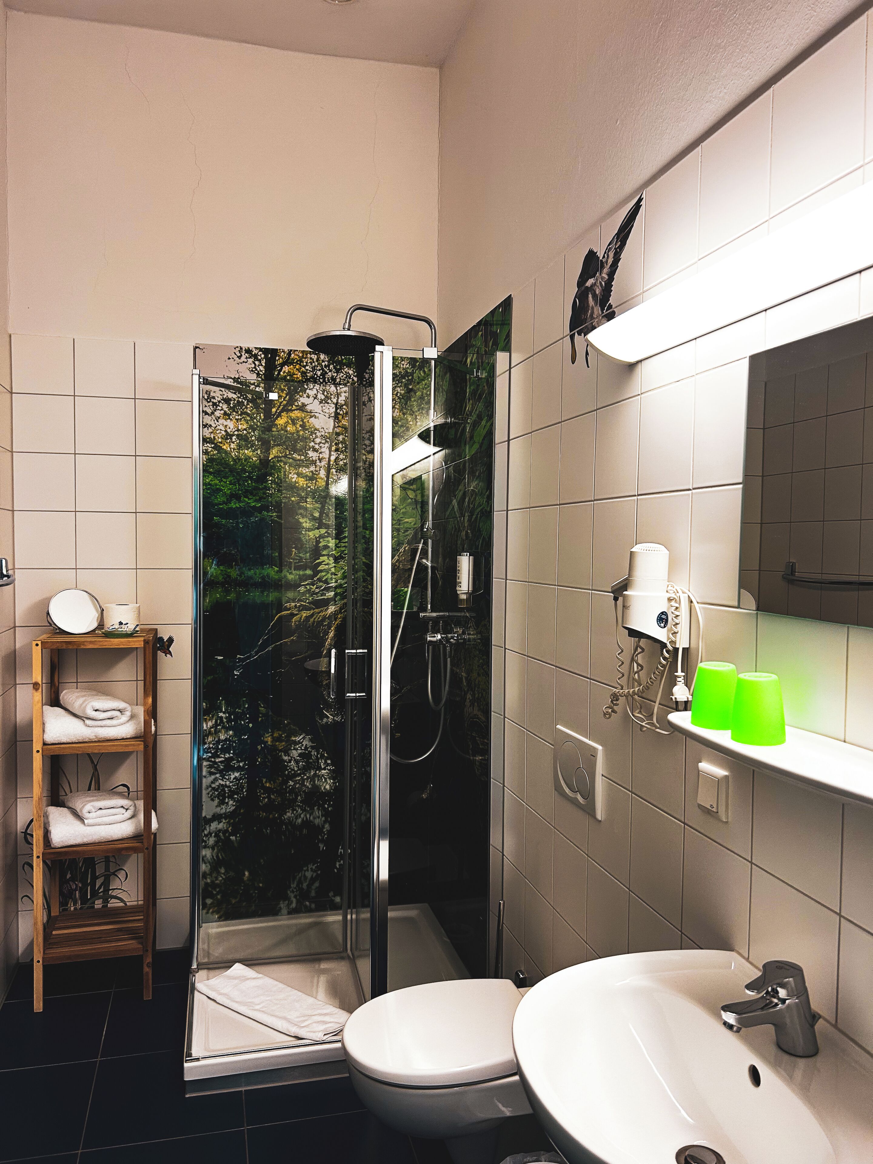 Un baño moderno con ducha envuelta en vidrio, inodoro, lavabo y estante de madera con toallas.