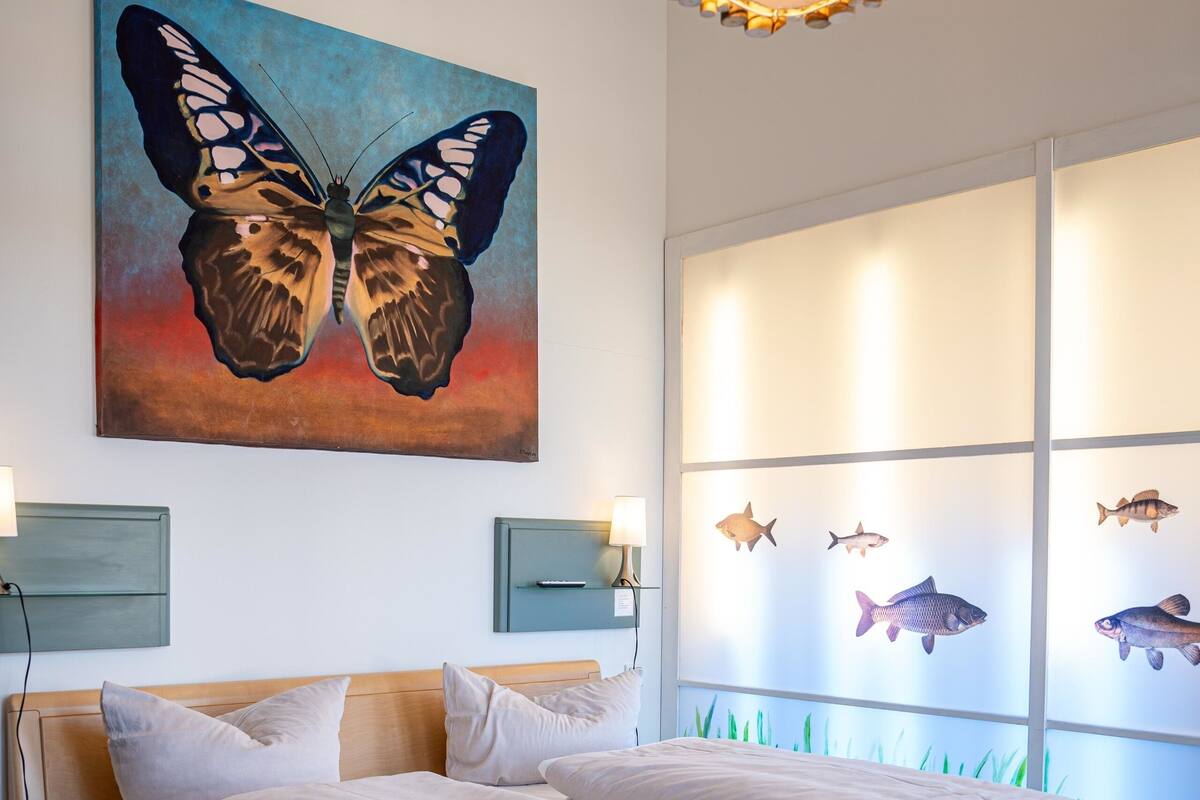 A bedroom with a bed, a wall-mounted painting of a butterfly, and a fish-themed window.