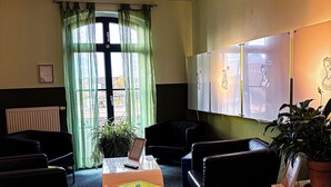 A waiting area with a reception desk, chairs, a potted plant, and a large window with curtains.