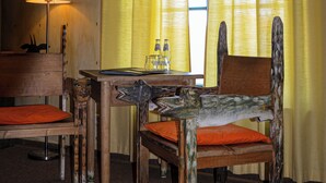 A room with a wooden table, two chairs, a lamp, and yellow curtains.