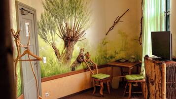 Una habitación con una cama, dos sillas, una mesita, un televisor y un mural en la pared.
