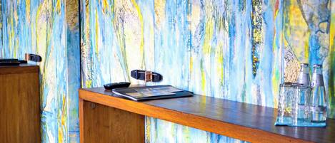 Une pièce avec un bureau en bois, deux chaises et une fresque murale abstraite et colorée.