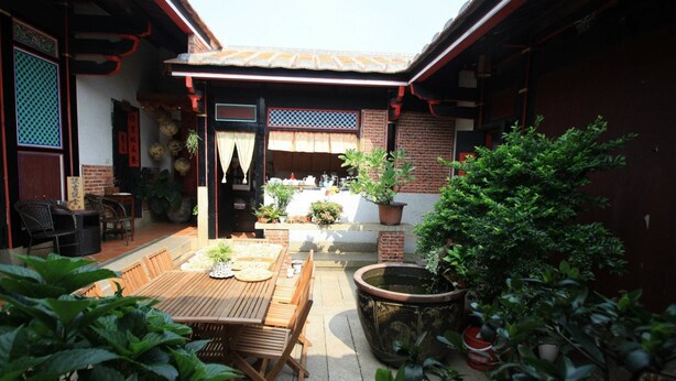 Ein traditioneller japanischer Innenhof mit Holztisch und -stühlen, Blumentöpfen und einem großen Wasserspiel.