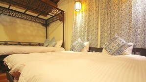 Ein Zimmer mit zwei Betten, jeweils mit Kopfteil und Kissen. Ein gemustertes Vorhang und eine Hängelampe befinden sich über den Betten.