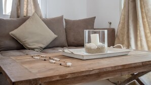 A wooden table with a glass container holding a candle and a tray with stones, placed on a sofa with beige cushions. - Villa Sofia, The Best SeaView Of Naxos (Νάξος)
