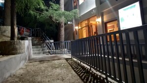 A building with a staircase leading to a door, a metal fence, and trees. - White Water Inn McLeodganj (Dharamshala)