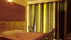 A room with a brick wall, a bed with a headboard, two chairs, and a window with yellow curtains. - White Water Inn McLeodganj (Dharamshala)