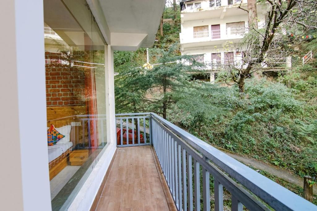 A balcony with a wooden floor and a white railing, overlooking a lush green area with trees and a building in the background.