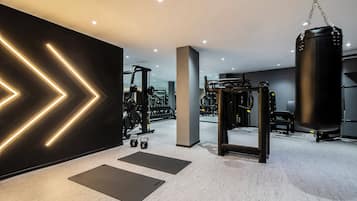 Un gimnasio moderno con equipo de ejercicio, colchonetas negras e iluminación de pared geométrica.