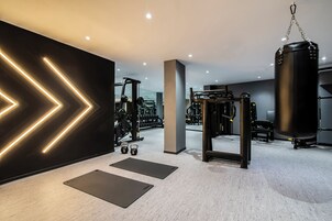 Un gimnasio moderno con equipo de ejercicio, colchonetas negras e iluminación de pared geométrica.