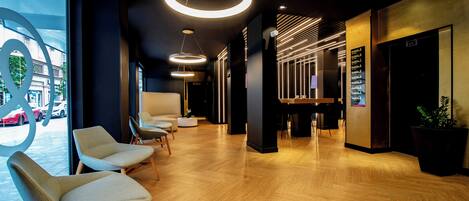 A modern lobby with wooden flooring, circular pendant lights, and a reception desk with a digital display.