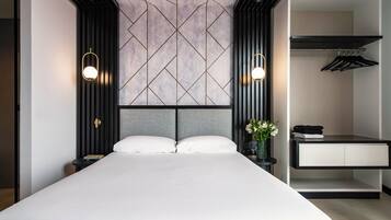 A modern hotel room with a large bed, a nightstand, a dresser, and a wardrobe.