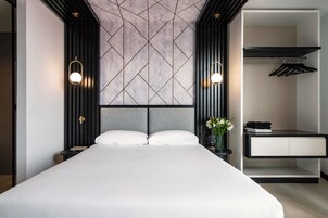 A modern hotel room with a large bed, a nightstand, a dresser, and a wardrobe.