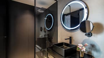 Ein modernes Badezimmer mit einer Duschkabine aus Glas, einem schwarzen Waschbecken und zwei wandmontierten Spiegeln mit beleuchtetem Rand.