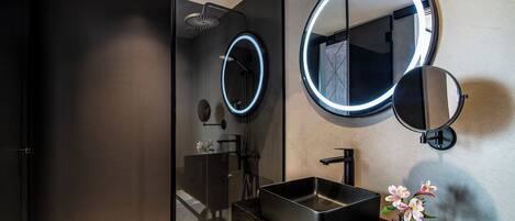 Une salle de bain moderne dotée d’une douche à parois de verre, d’un lavabo noir et de deux miroirs muraux aux bords éclairés.