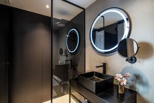 Ein modernes Badezimmer mit einer Duschkabine aus Glas, einem schwarzen Waschbecken und zwei wandmontierten Spiegeln mit beleuchtetem Rand.