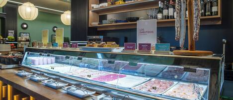 Mostrador de delicatessen con diversos tipos de embutidos y quesos, una estantería con vino arriba y un letrero que indica fiambres.