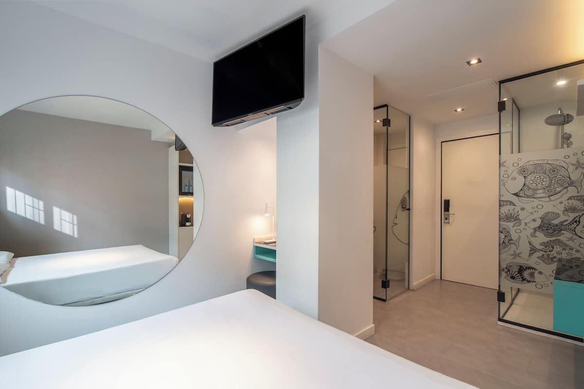 A modern bedroom with a bed, a large mirror, a television, and a shower area.