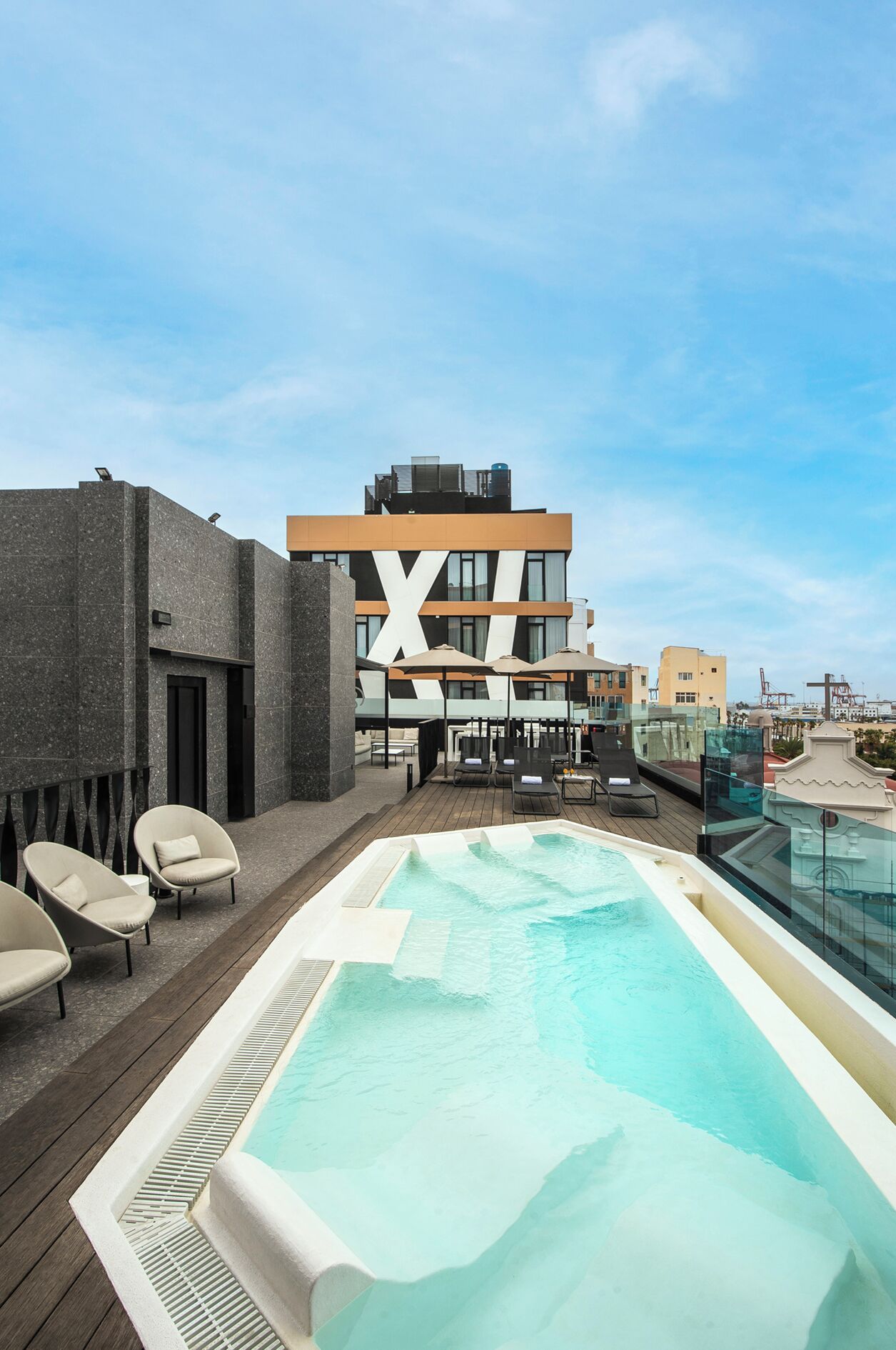 A rooftop pool area with lounge chairs and a large building in the background.