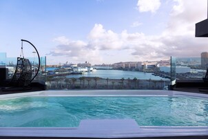 Una piscina infinita en la azotea con vistas a la ciudad, incluyendo un puerto deportivo y edificios.