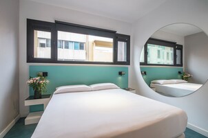 Una habitación de hotel moderna con una cama grande, un espejo y una ventana con vistas a edificios.