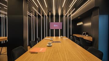 Una sala conferenze con un lungo tavolo, sedie, uno schermo e una scrivania con un portatile.
