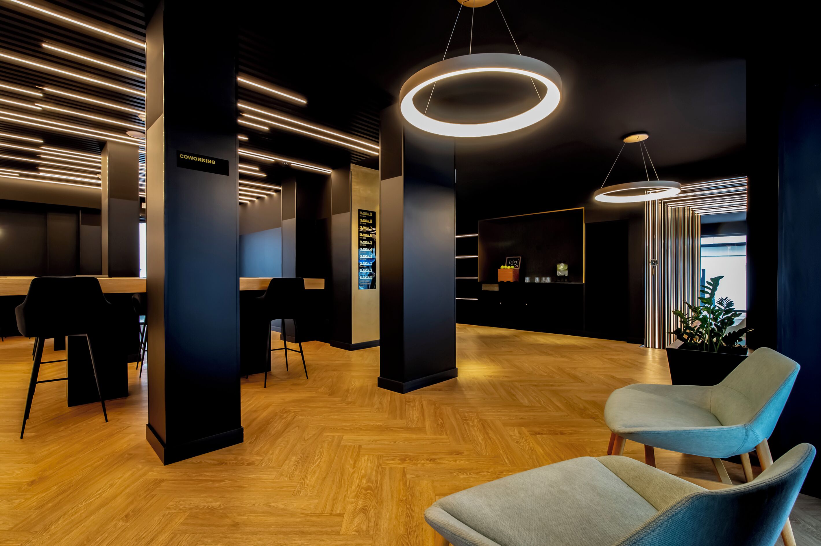 Un espace de travail partagé moderne, doté de planchers en bois, de meubles noirs et gris, et d’un panneau indiquant l’emplacement de la zone de coworking.