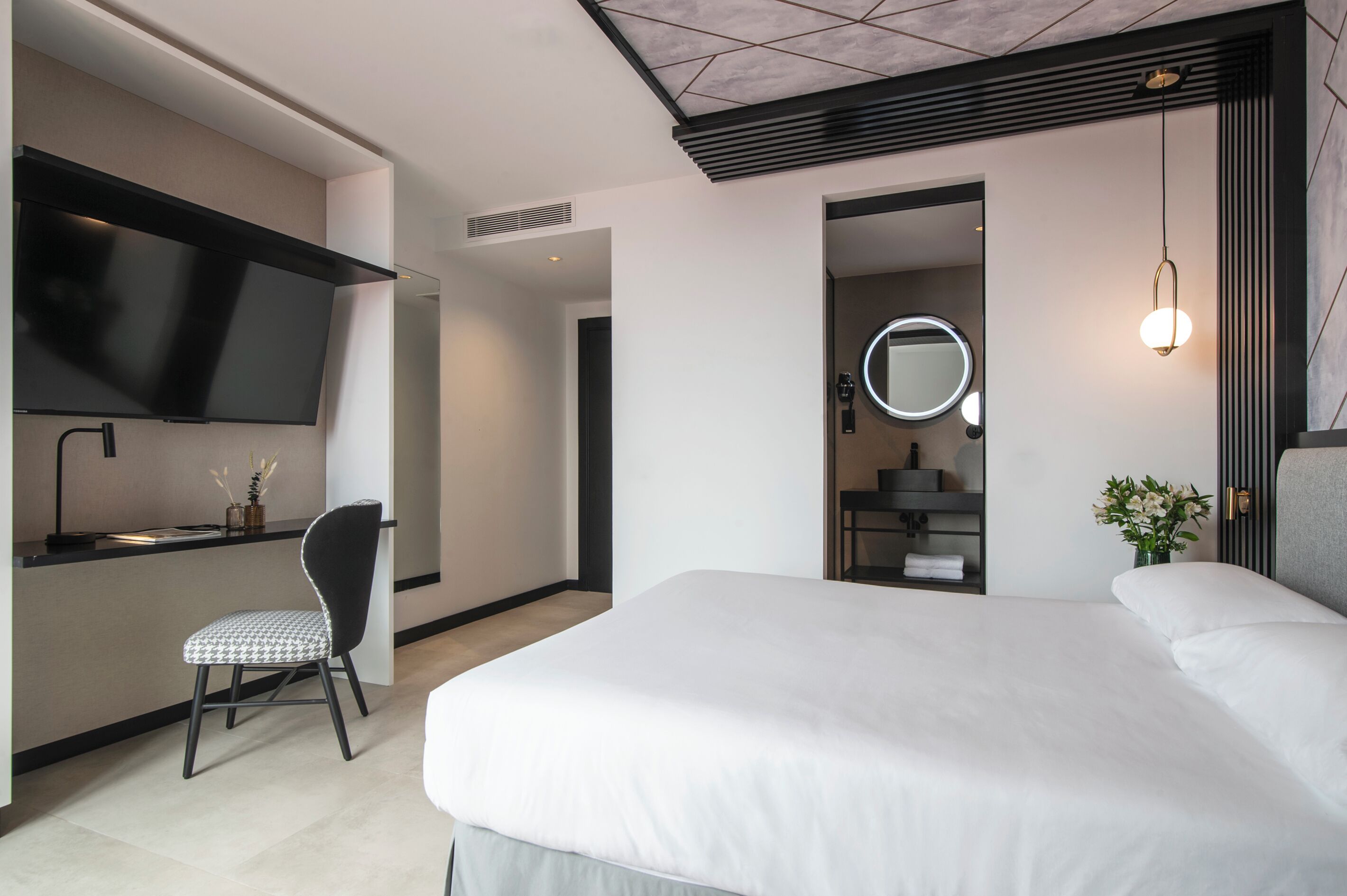 Een moderne hotelkamer met een groot bed, een bureau met stoel, een televisie, een spiegel en een kleine plant.