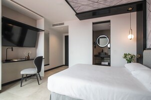 Une chambre d’hôtel moderne, dotée d’un grand lit, d’un bureau avec une chaise, d’une télévision, d’un miroir et d’une petite plante.