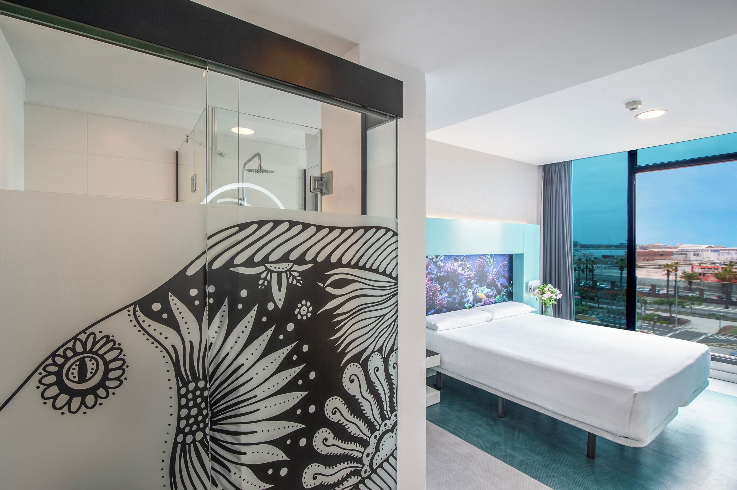 Quarto de hotel moderno com uma cama grande, chuveiro de vidro e vista para a cidade.