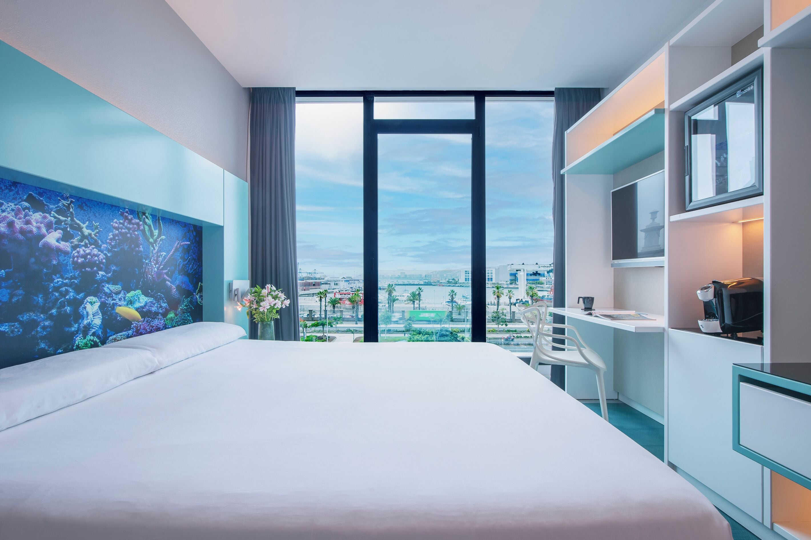 Habitación de hotel moderna con una cama grande, un escritorio y vistas a la ciudad a través de amplias ventanas.