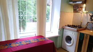 Une cuisine compacte équipée d’un lave-linge, d’un petit plan de travail et d’une fenêtre avec des rideaux.
