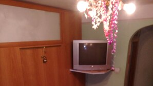 Une pièce avec une armoire en bois, un téléviseur posé sur un meuble et une petite boîte en bois sur le sol.