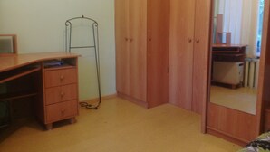 Une chambre avec une armoire en bois, un bureau avec des tiroirs, un radiateur et un miroir.