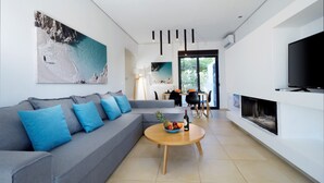 A modern living room with a grey sofa, a round wooden coffee table, and a large TV screen. - Seametry Villa (Νεροκουρος)