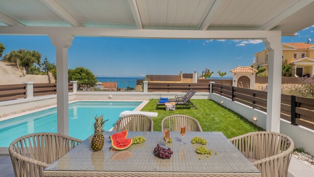 Un espacio al aire libre techado con piscina, mobiliario de mimbre y una mesa dispuesta con frutas y bebidas.