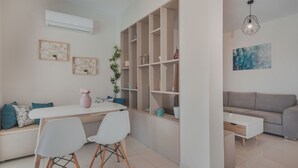 Una sala de estar moderna con un sofá blanco, una mesa de comedor con dos sillas, una estantería y un sofá gris.