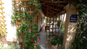 Un espacio de estar al aire libre cubierto, con una pérgola de madera, plantas en macetas y un cartel que indica que es un apartamento.