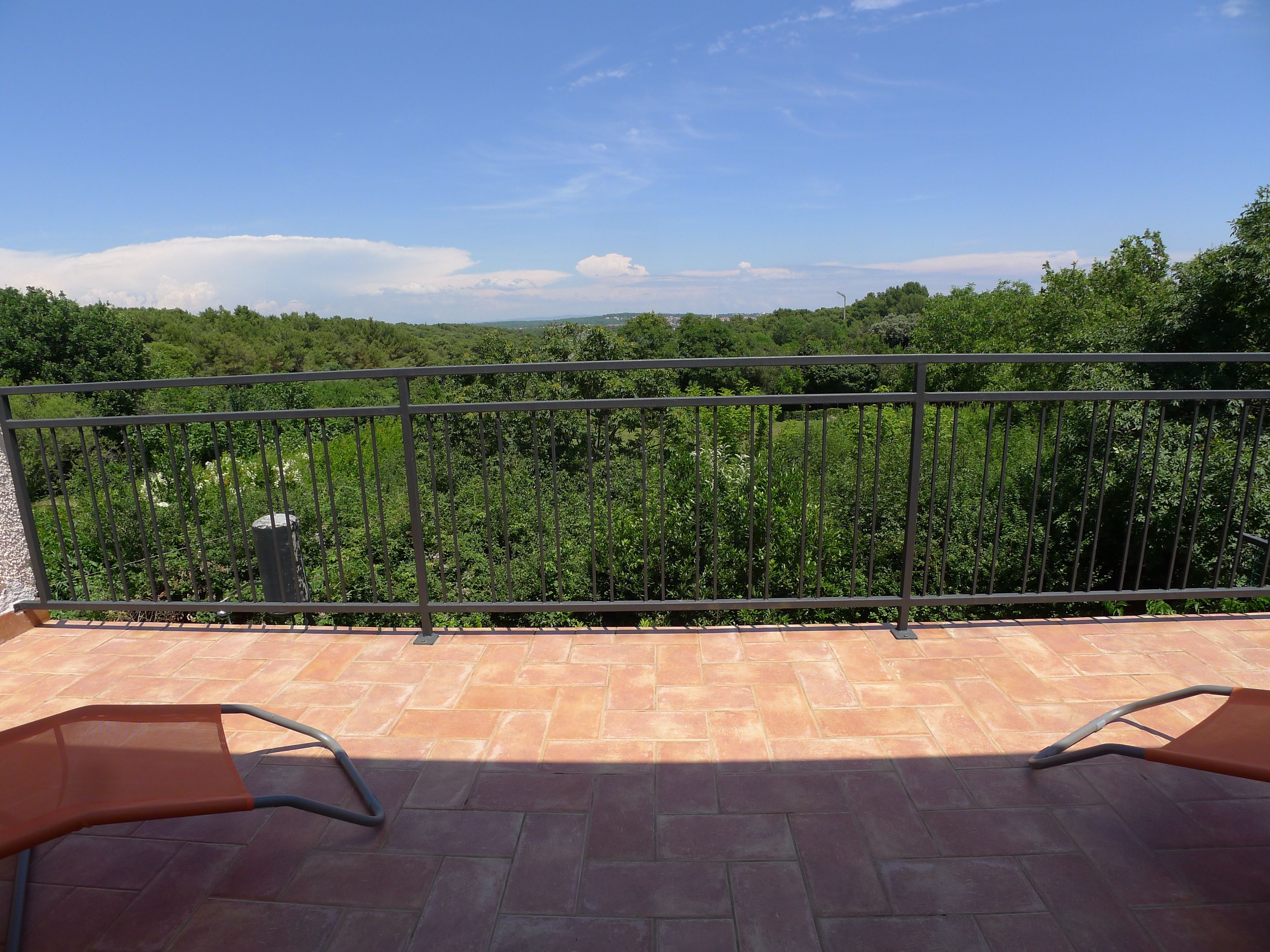 Un balcón con vistas a una zona boscosa, suelo de baldosas y dos sillas.