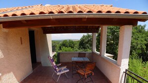 A covered outdoor patio with a table and chairs, a view of the surrounding greenery, and a tiled roof. - Apartment for 3 Persons in Quiet Part of Premantura With Beautiful Garden and Partial sea View (Medulin)