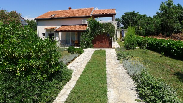A two-story house with a tiled roof, a stone pathway leading to the entrance, and a well-maintained garden. - Apartment for 3 Persons in Quiet Part of Premantura With Beautiful Garden and Partial sea View (Medulin)