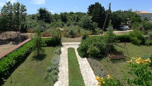A garden with a stone pathway, a swing set, and a car parked in the background. - Apartment for 3 Persons in Quiet Part of Premantura With Beautiful Garden and Partial sea View (Medulin)