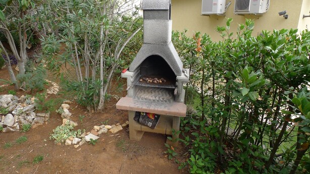 A stone-built outdoor oven with a chimney, surrounded by greenery and a tiled-roofed building. - Apartment for 5 Persons With two Bedrooms and Internet (Medulin)