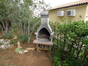 A stone-built outdoor oven with a chimney, surrounded by greenery and a tiled-roof building. - Apartment for 5 Persons With two Bedrooms and Internet (Medulin)