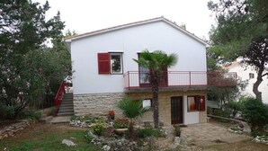 A two-story house with a stone base and white upper walls, a red balcony, and a small garden with various plants and flowers. - Apartment for 5 Persons With two Bedrooms and Internet (Medulin)