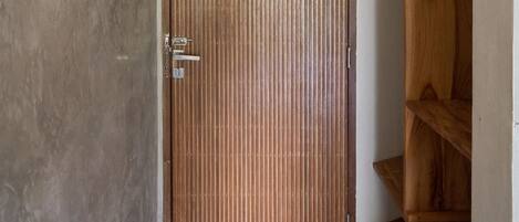 A room with a wooden door, a white air conditioning unit above it, and a wooden shelf to the right.